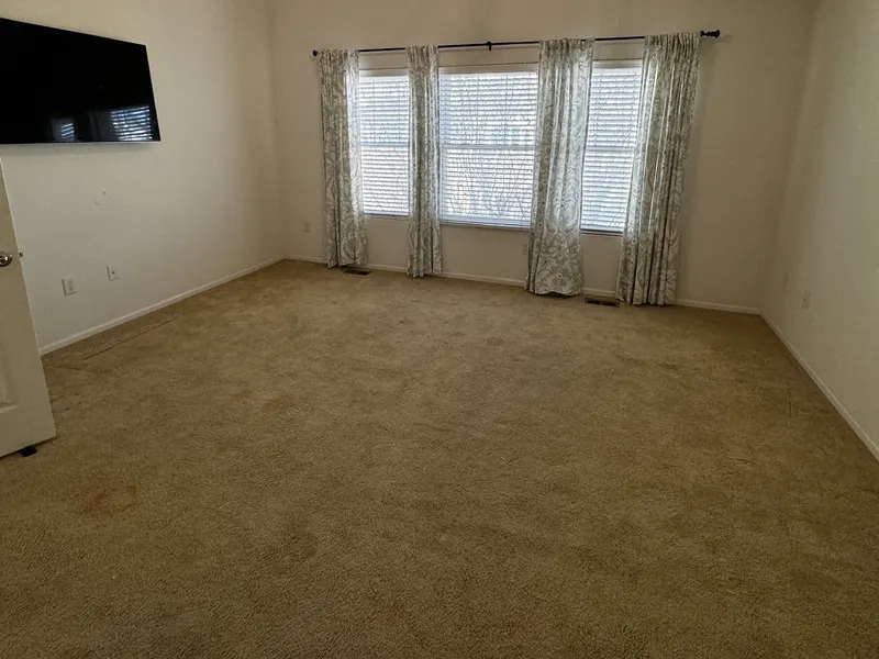Primary bedroom before prep: dated carpet and heavy patterned curtains